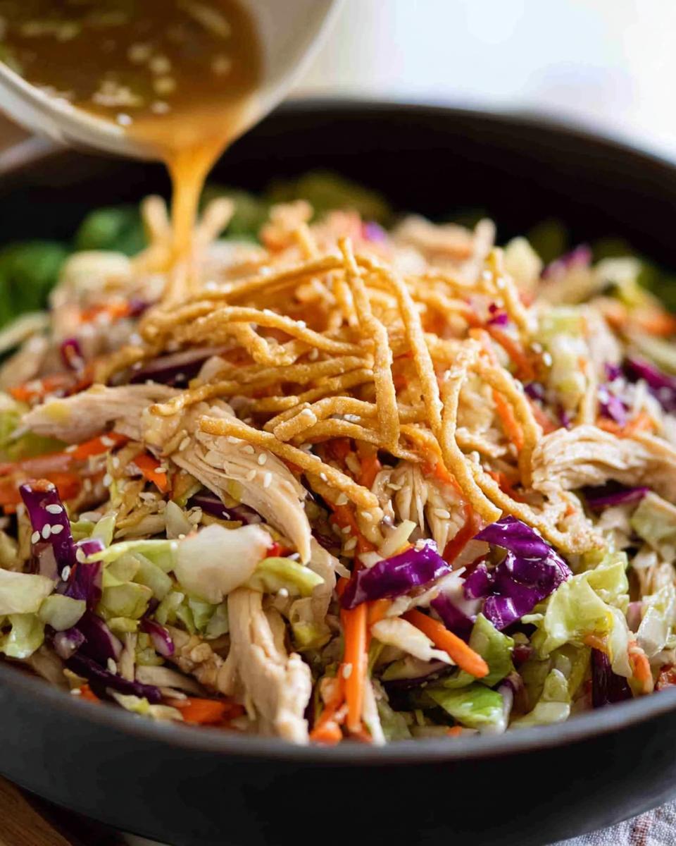 15-Minute Chinese Chicken Salad with Sesame Dressing 4 Pouring sesame dressing over a vibrant Chinese Chicken Salad with shredded chicken, cabbage, carrots, and crispy noodles.