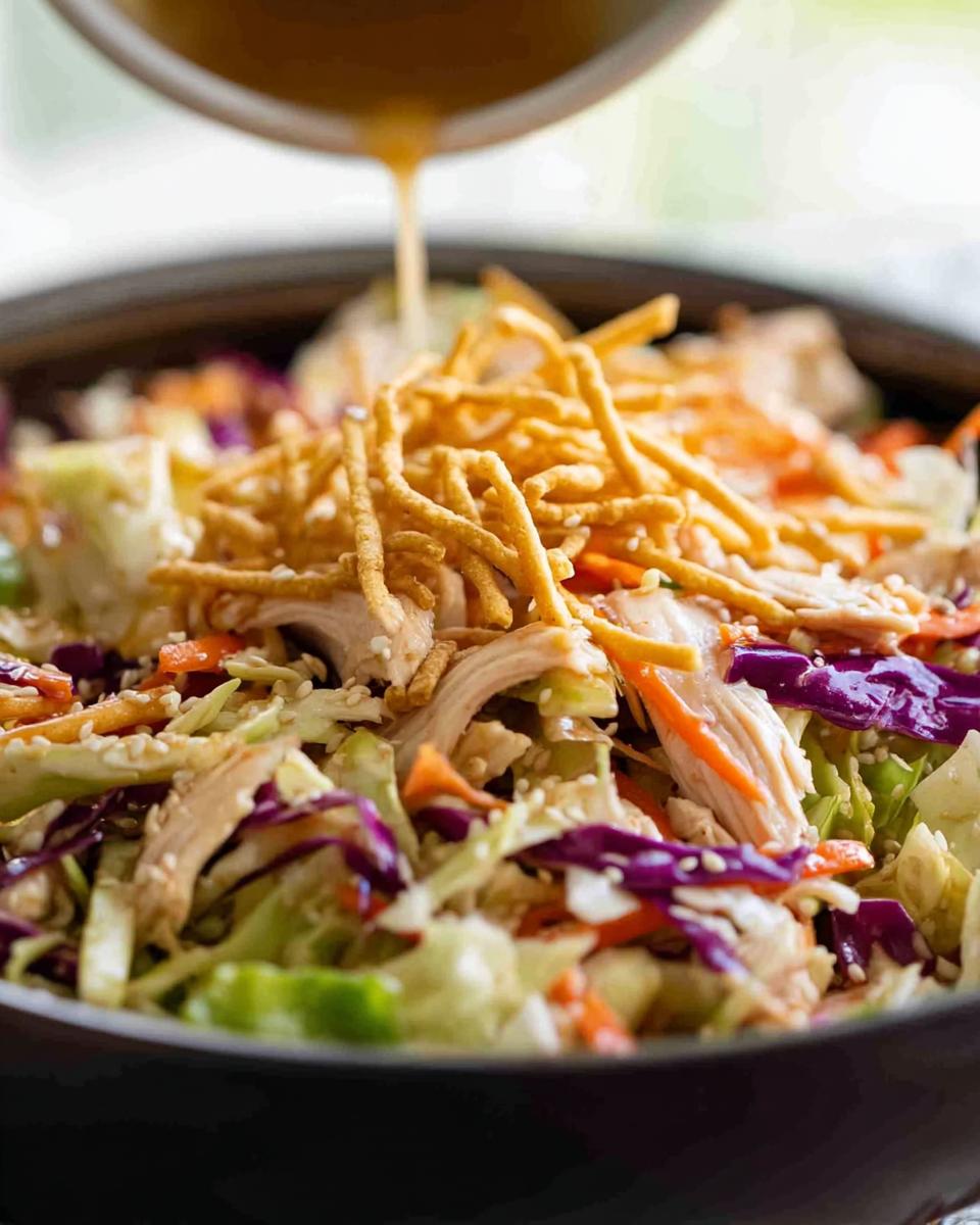 15-Minute Chinese Chicken Salad with Sesame Dressing 5 Pouring sesame dressing over a fresh Chinese Chicken Salad with shredded chicken, cabbage, carrots, and crunchy noodles.