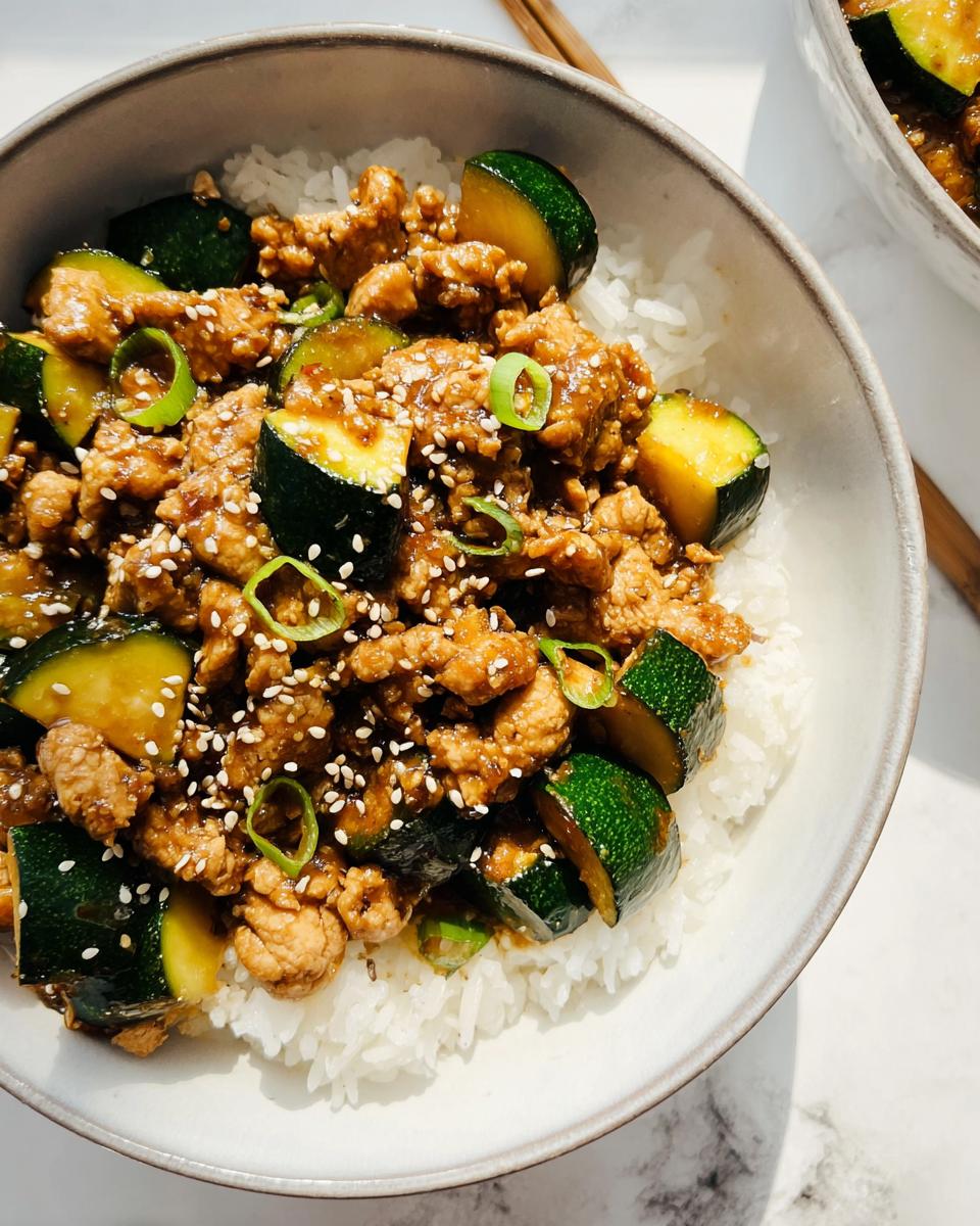 Savor Our 30-Minute Garlic Ginger Chicken Zucchini Stir Fry 4 A close-up of Garlic Ginger Chicken Zucchini Stir Fry served over fluffy white rice, garnished with sesame seeds and green onions.