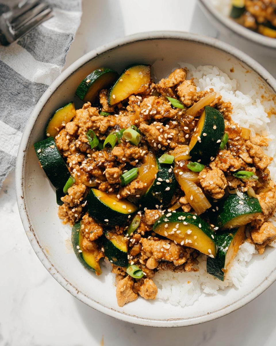 Savor Our 30-Minute Garlic Ginger Chicken Zucchini Stir Fry 5 A close-up of Garlic Ginger Chicken Zucchini Stir Fry served over white rice in a bowl, garnished with sesame seeds and green onions.