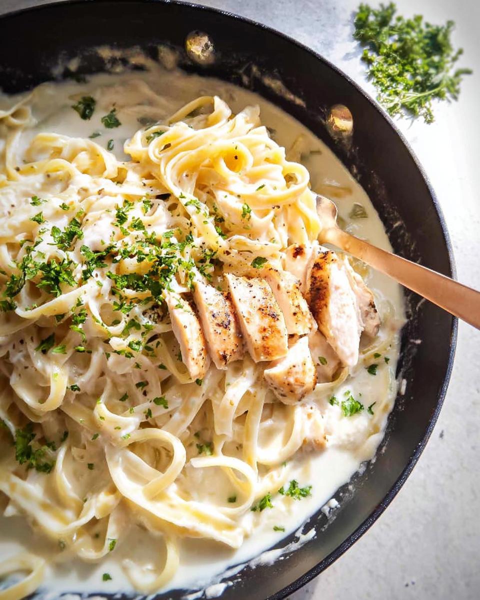 One Pot Creamy Chicken Alfredo Pasta: 30 Minute Magic 4 Close-up of One Pot Creamy Chicken Alfredo Pasta in a black skillet, topped with sliced chicken and parsley.