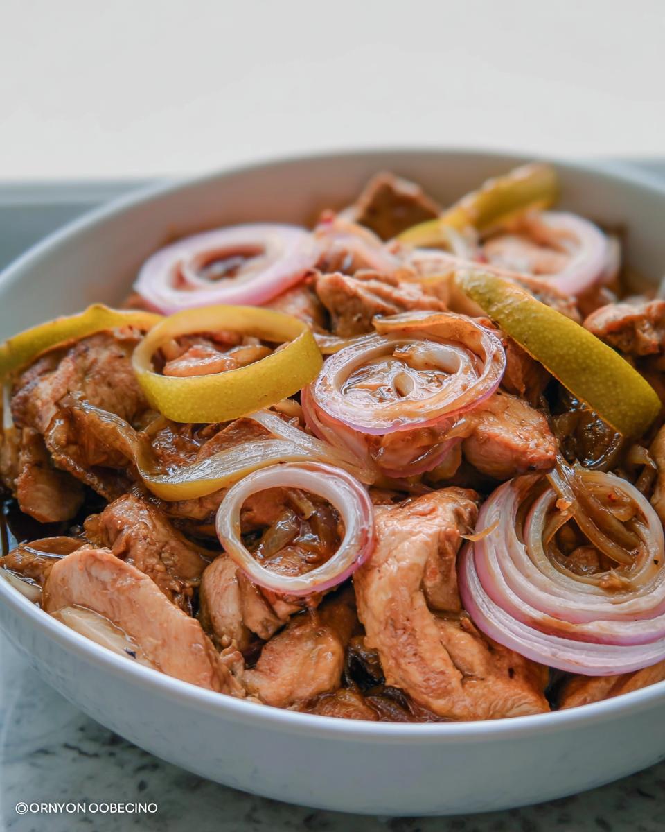 Amazing Easy Chicken Bistek: 30 Min Flavor 5 Close-up of Easy Chicken Bistek with Onions, featuring tender chicken pieces, caramelized onions, and lemon slices in a white bowl.