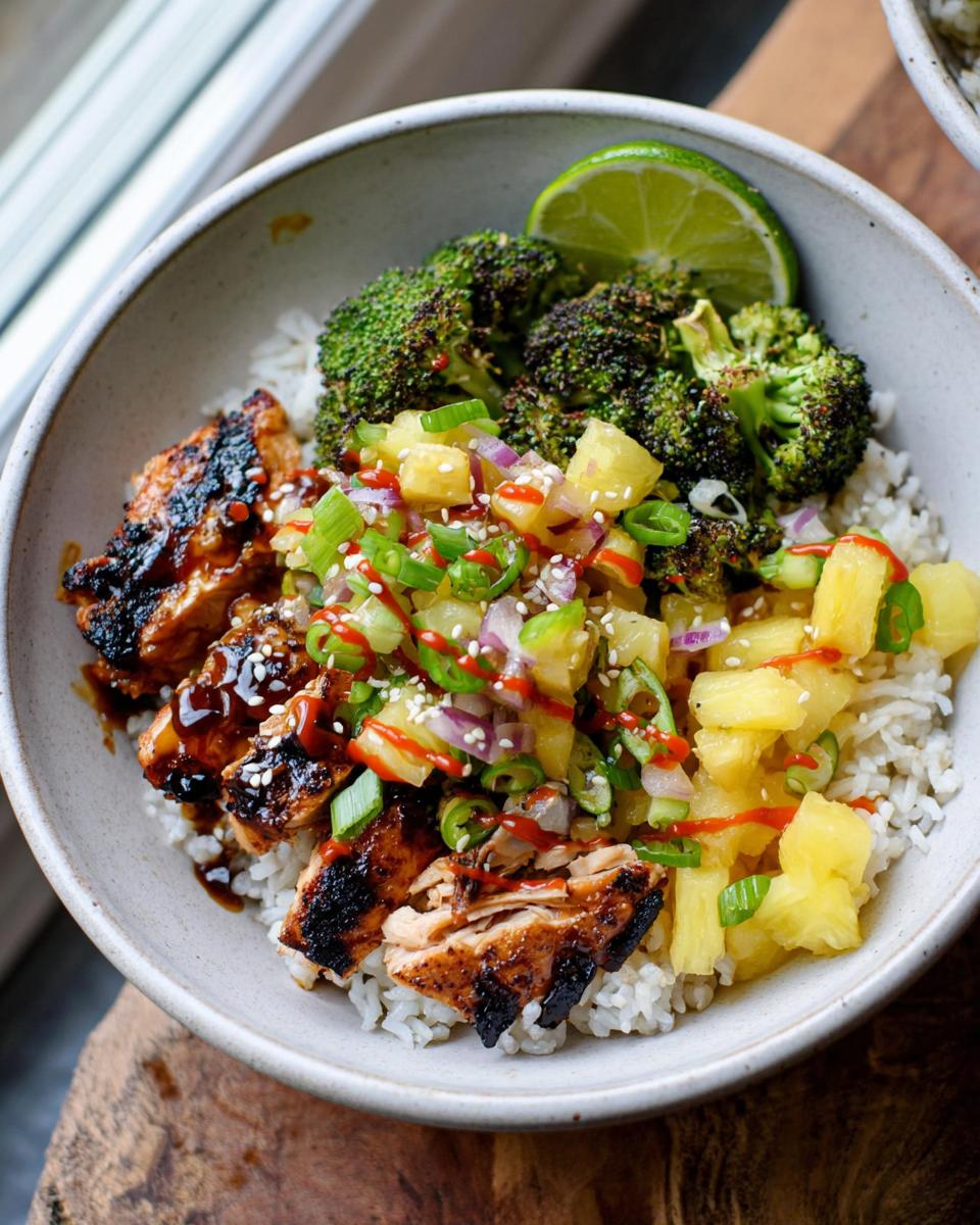 Amazing 30-Min Huli Huli Chicken Rice Bowls 4 A close-up of a Huli Huli Chicken Rice Bowl featuring grilled chicken, rice, roasted broccoli, pineapple salsa, and a lime wedge.